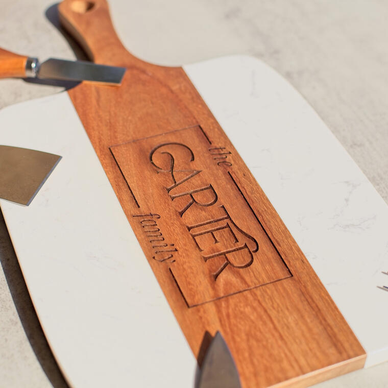 Custom laser-engraved wood and marble serving board featuring 'The Carter Family' personalization. An elegant housewarming gift or realtor closing gift, showcasing deep-etch wood engraving on a high-quality charcuterie paddle with white marble accents.